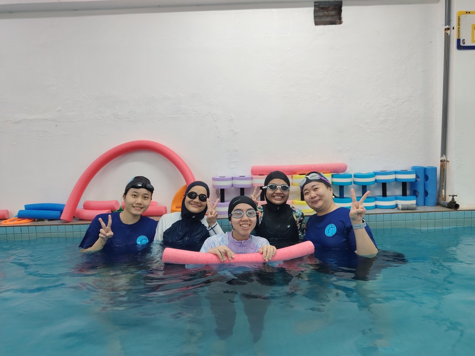 A coach working closely with a small private group, using pool noodles for support during a 1-to-1 session