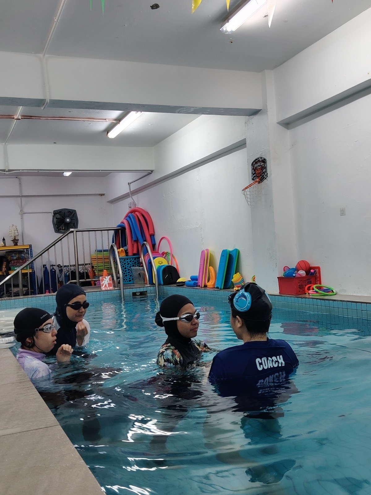 A coach teaching a small group of adult students in the warm indoor pool